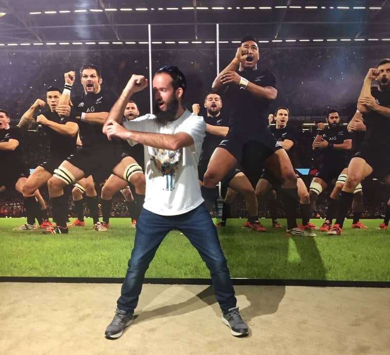 jub pretending to do the haka with the wall in the background showing a large photo of the All Blacks doing the haka