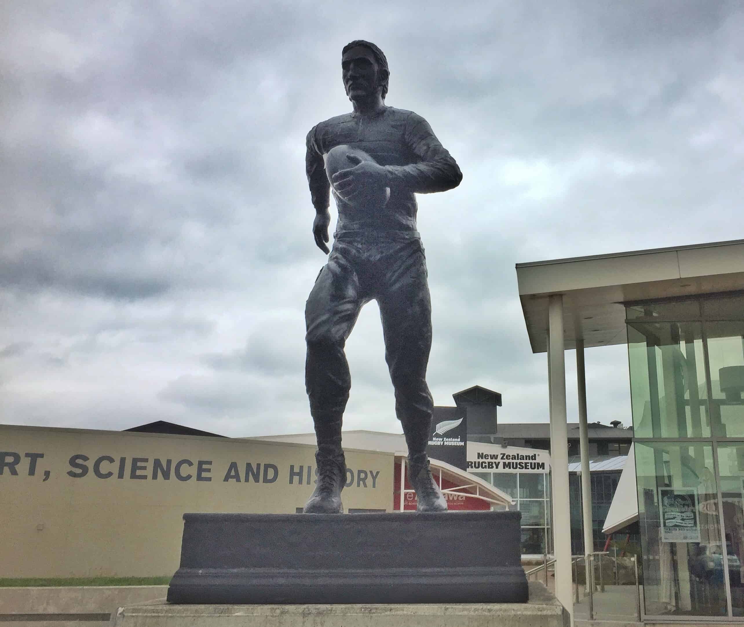 a statue of charles munro running with a rugby ball in front of the New Zealand rugby museum building