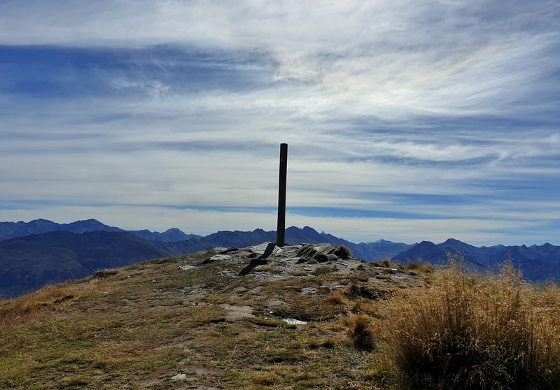 a pole in the ground marking the summit of isthmus peak with clouds in the background