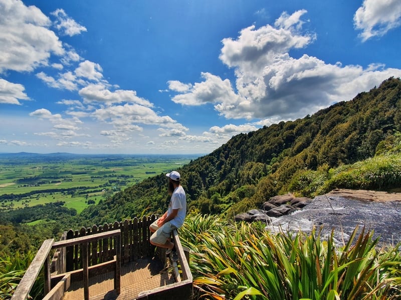 man sitting on a platform at the top of the wairere falls walk looking over the countryside.