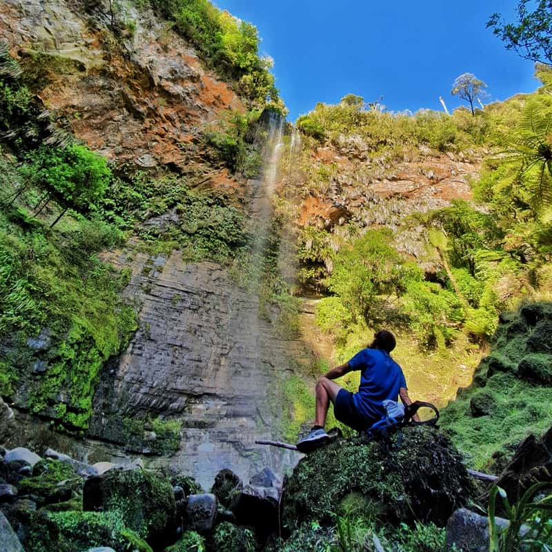 man sitting on rock below tupapakurua falls