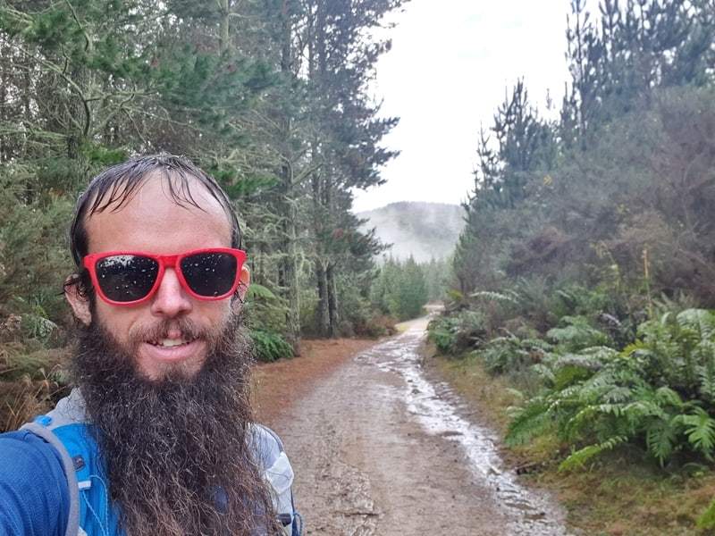 man taking a selfie with a muddy track and forest in the background