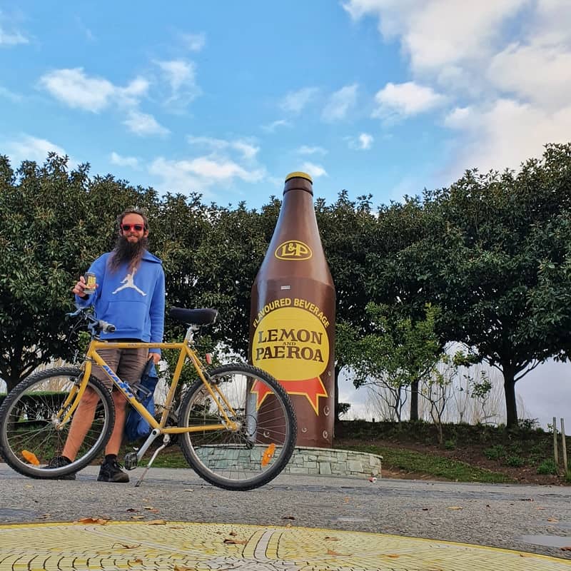 man with bike in front of iconic lemon and paeroa monument
