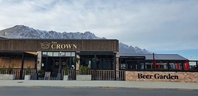a building that mentions the crown and beer garden with a mountain range in the background with cloudy skies