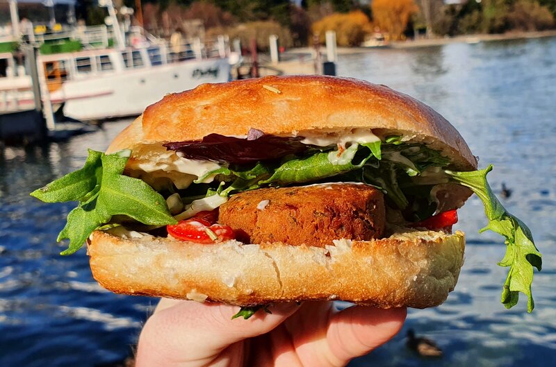 a bagel with vegetables and falafel being held in a hand