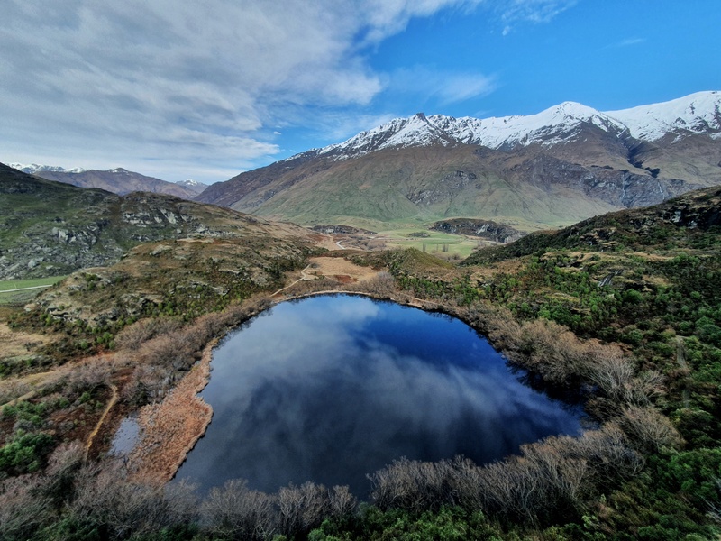 wide angle view of a lake from above. Mountain and cloudy sky in the background.