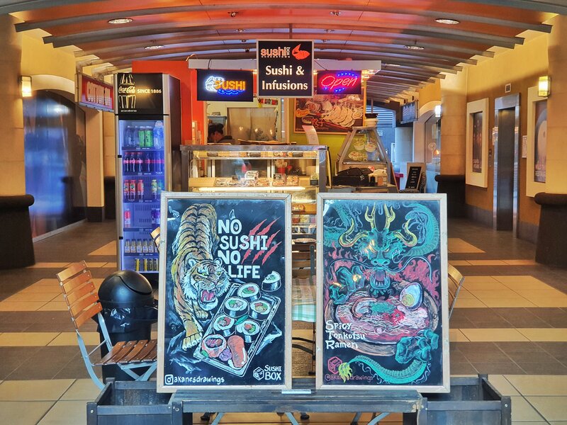 two signs in front of a sushi shop inside a shopping mall