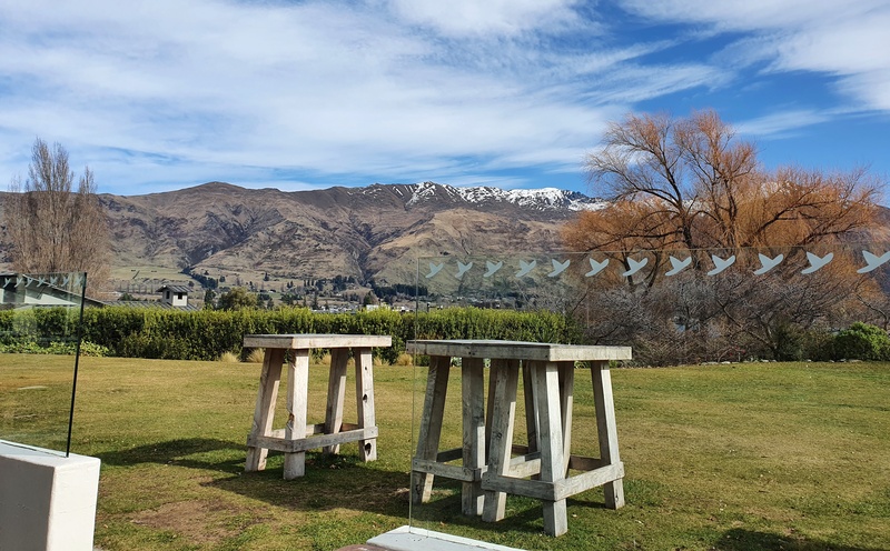 two wooden tables on glass with a mountain range in the background. cloudy blue sky.