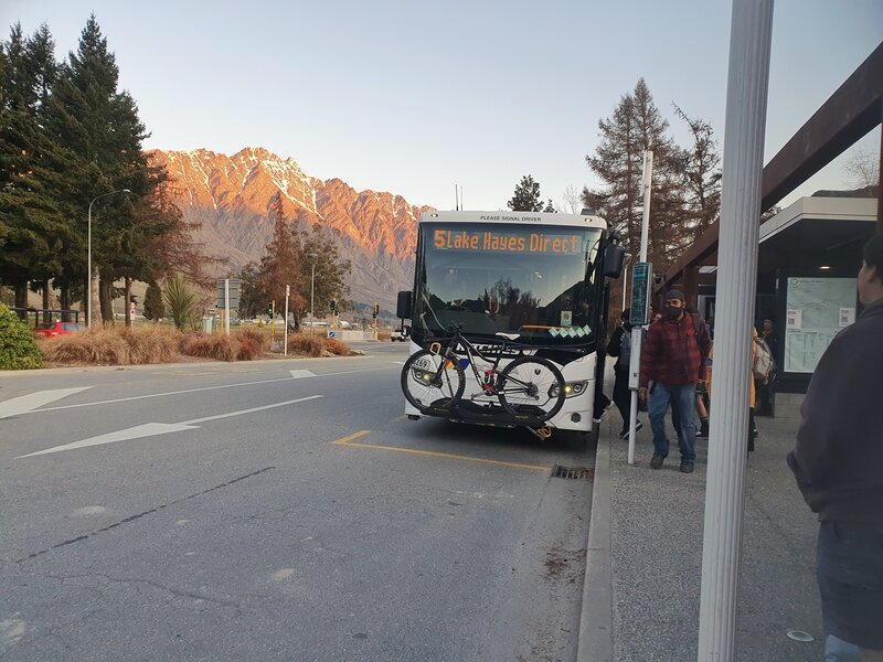 a bus with a bike on the front waiting at a bus stop while people get on