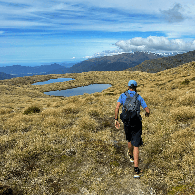 man hiking towards two tarns on a sunny day with the OMM classic 32 backpack